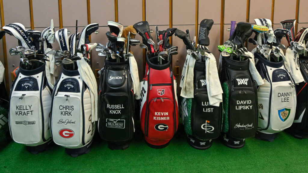 a selection of tour player golf bags lined up in a locker room