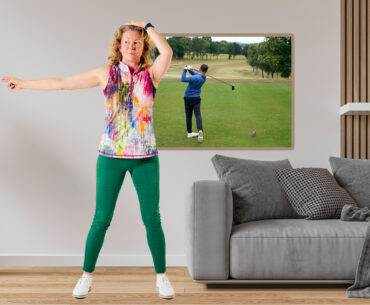 Katie Dawkins demonstrating the shoulder turn drill that can power up your golf swing at home in just five minutes, in a living room setting in a modern house, with a picture frame on the wall showing Baz Plummer hitting a driver at Sand Moor Golf Club