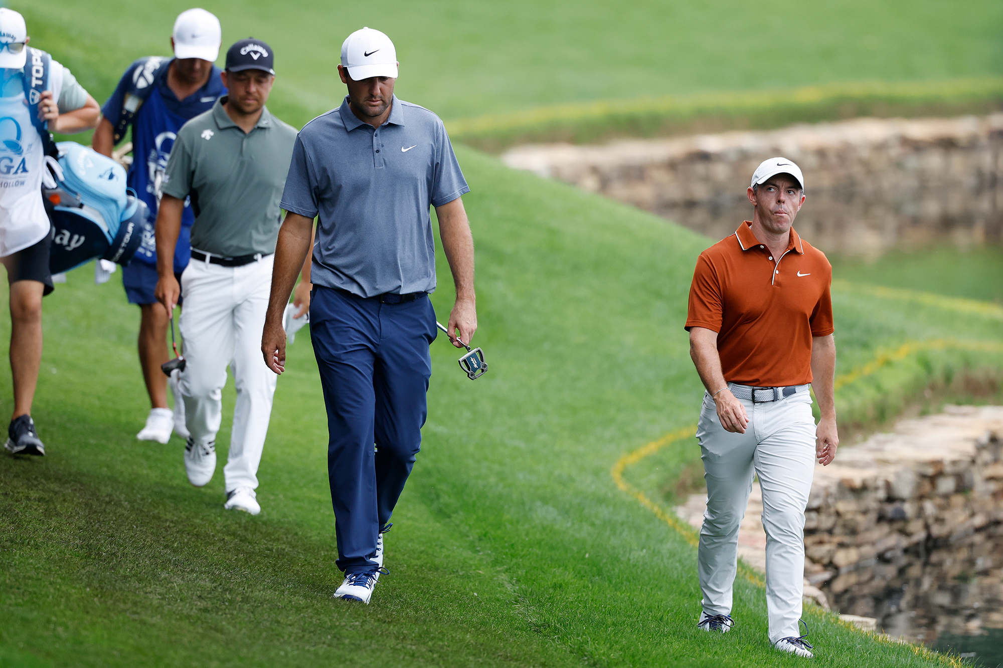 Scottie Scheffler, Rory McIlroy and Xander Schauffele, the featured group at the 2025 PGA Championship, walking towards the putting green at Quail Hollow holding their putters