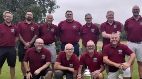 Contributed The Beccles Golf Club team smile after winning their competition. There are 11 men all wearing the same red polo T-shirt. Stuart Hagger sits on the bottom row crouching. He hold the trophy. 