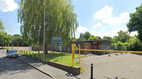 Google A building set back from the road, with grass and a Brandhall Golf Course sign between the building and the street. The building has been fenced off.