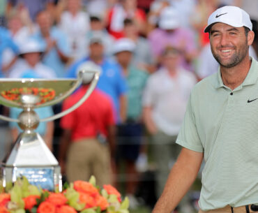 Scottie Scheffler smiles (right) with the FedEx Cup out of focus on the left