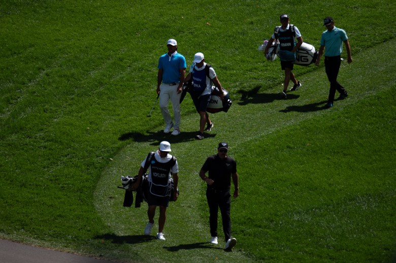 Golfers and caddies walk down a grass hill.