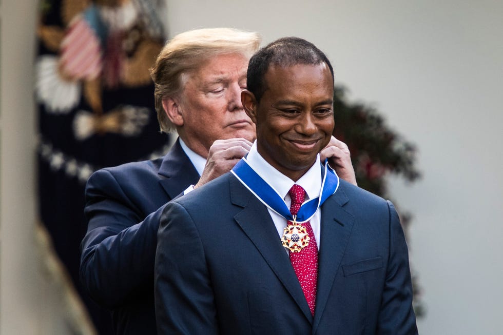 donald trump placing a medal around the neck of tiger woods as he stands behind him