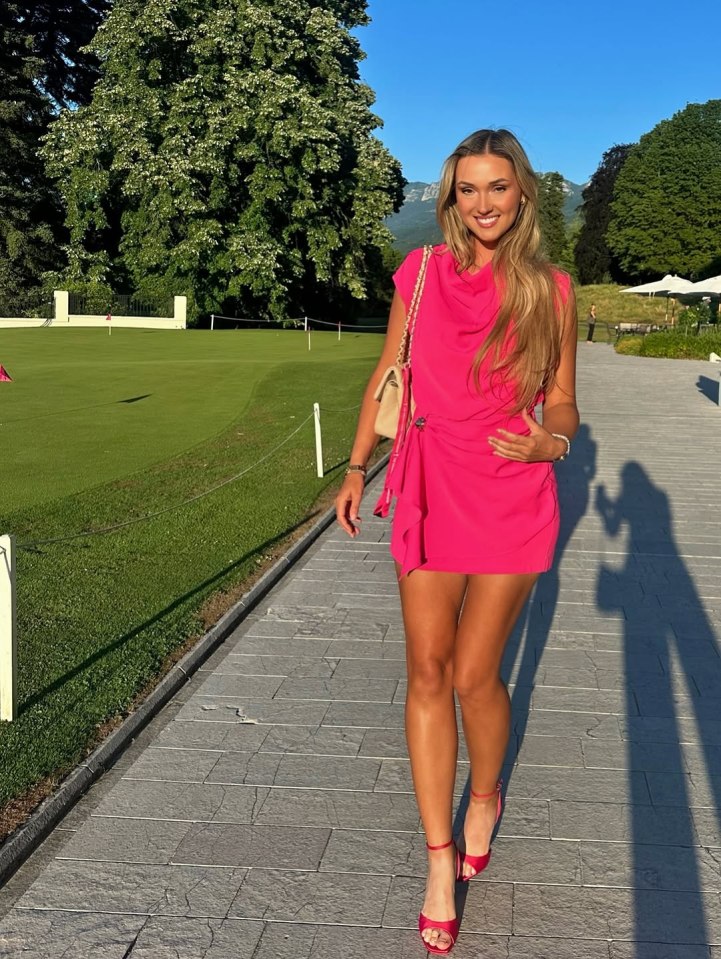 Woman in pink dress walking on path near golf course.