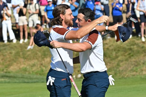 Europe's Northern Irish golfer, Rory McIlroy (R) is embraces by Europe's English golfer, Tommy Fleetwood (L) after holing his putt to win the hole and the match on the 17th green during his foursomes match on the second day of play