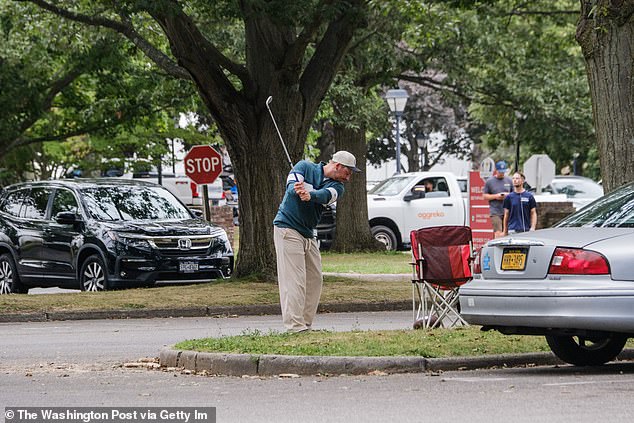 An amateur player practices his swing on a patch of grass in the parking lot at Bethpage