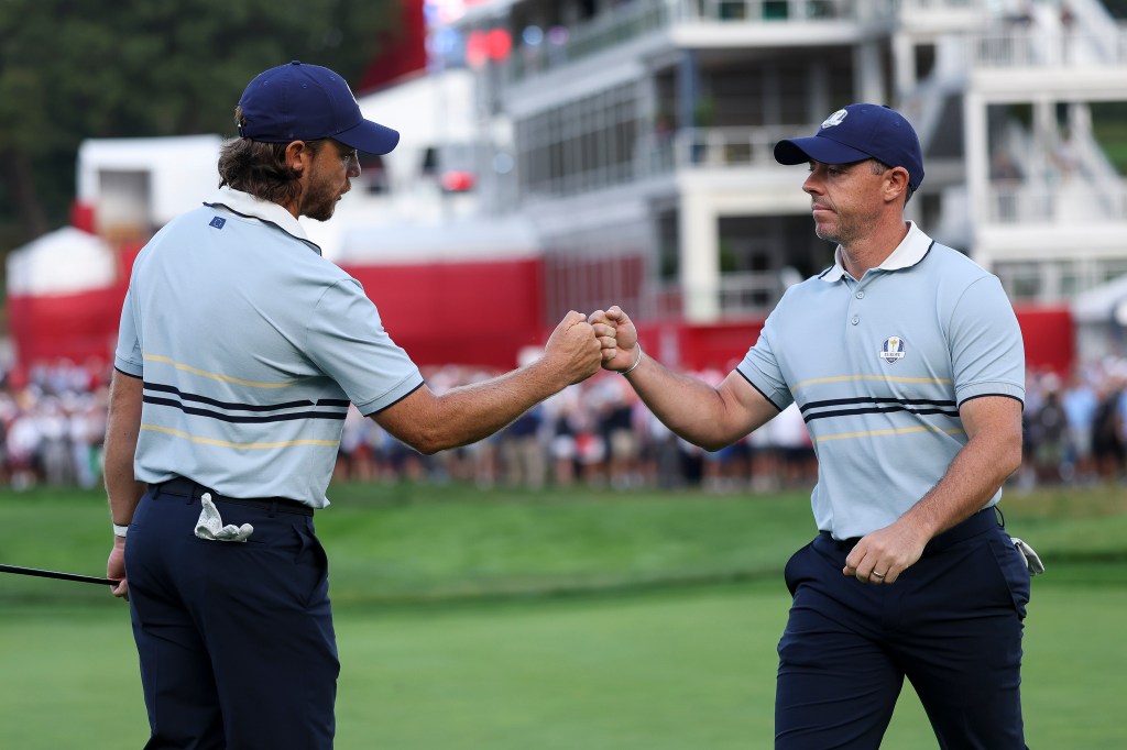 Tommy Fleetwood fist bumps teammate Rory McIlroy of Team Europe on the first green during the Friday morning foursomes matches of the 2025 Ryder Cup at Black Course at Bethpage State Park Golf Course on September 26, 2025 in Farmingdale, New York.