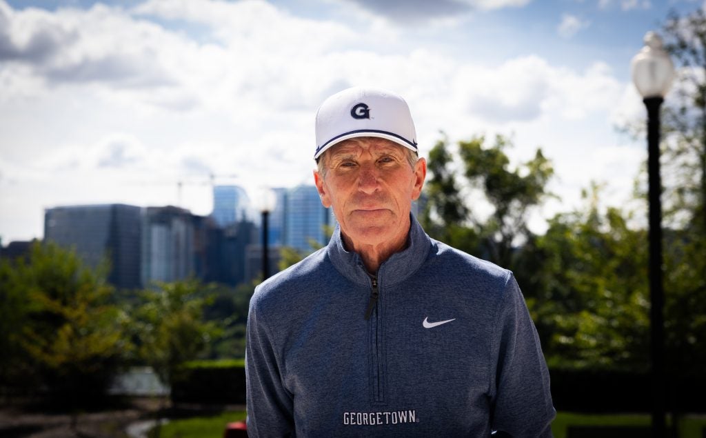Older Caucasian man in a blue pullover and white GU hat