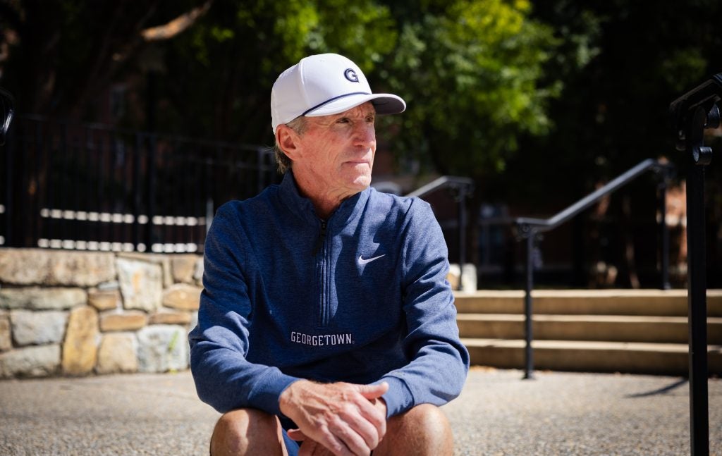 A man in a baseball cap and blue pullover looks into the distance while sitting on a step