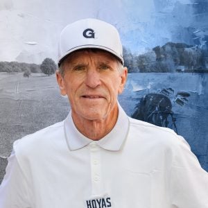 A man wears a white baseball hat with a "G" on it and a white polo shirt in front of a golf course background.