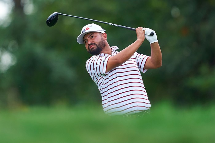 J.J. Spaun, in white, blue and red striped Team USA golf gear and a white cap, hits a golf shot at the Ryder Cup.