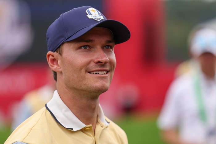 Rasmus Højgaard, in white and yellow Team Europe golf gear and a blue cap, smiles at the Ryder Cup 2025.