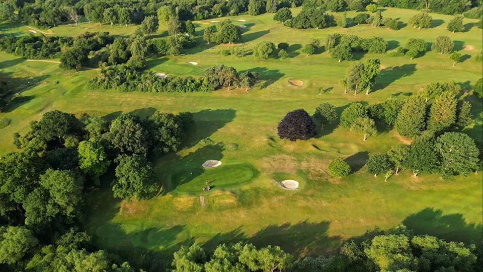 An aerial shot of Oxford Golf Club. The greens are well kept, and there are large sections of fairway. There are trees across the course.