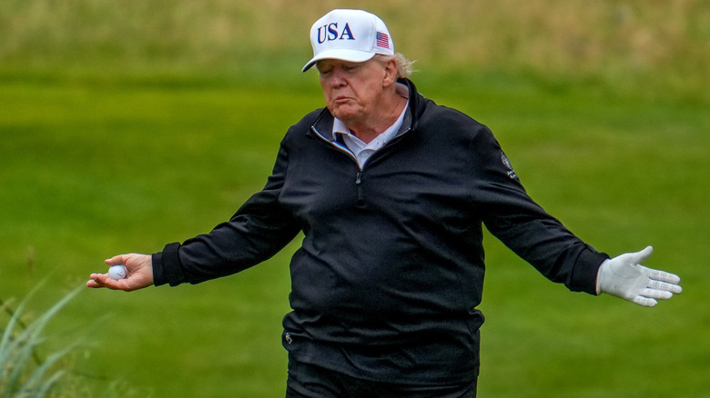 Donald Trump on golf course arms spread holding ball