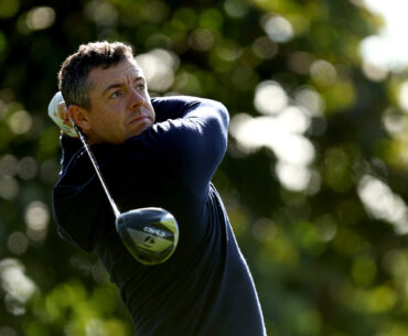 Rory McIlroy holds his finish on a drive wearing a navy hoody and no cap