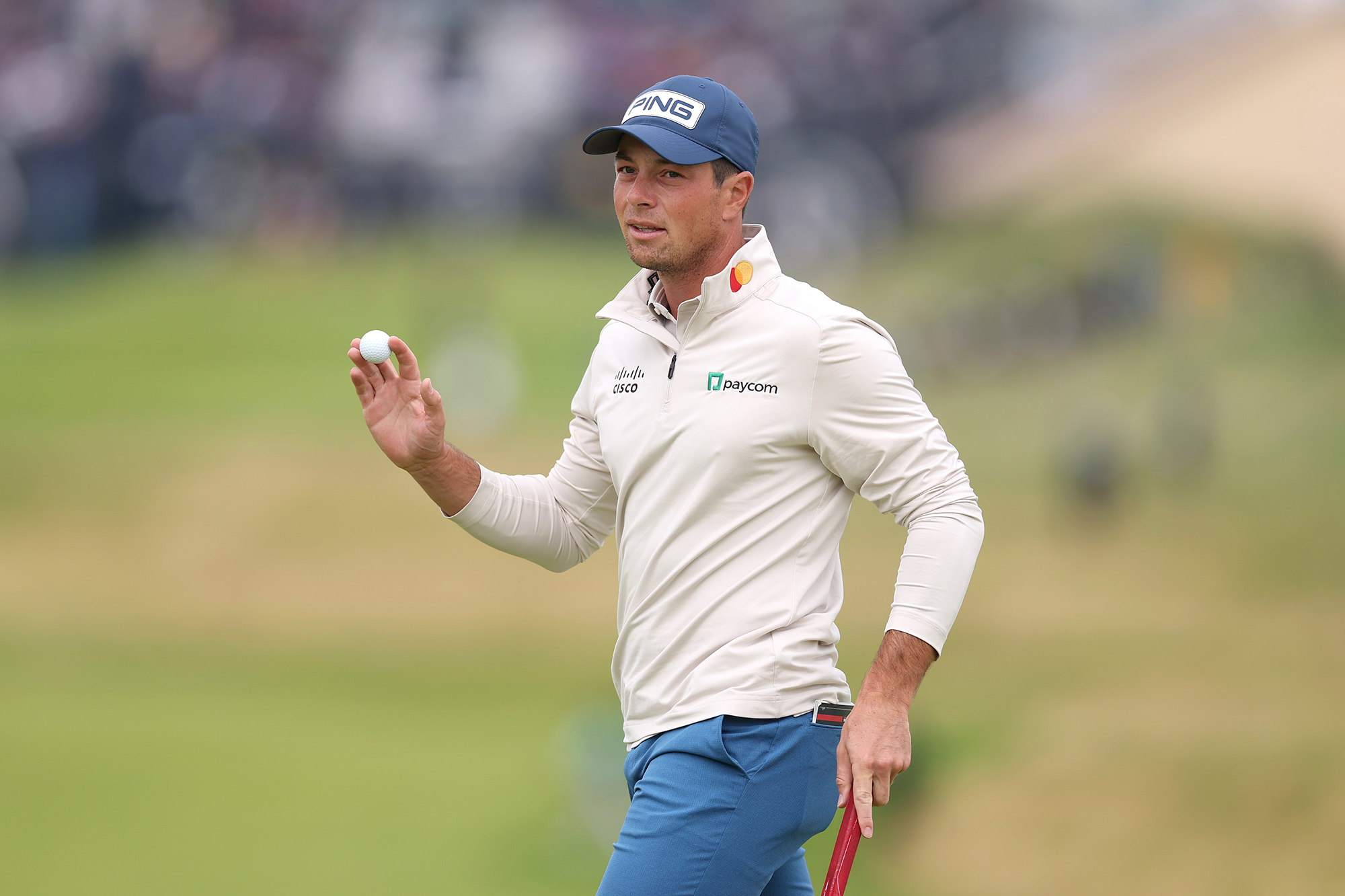 Viktor Hovland thanking the crowd by raising his golf ball after putting on the green