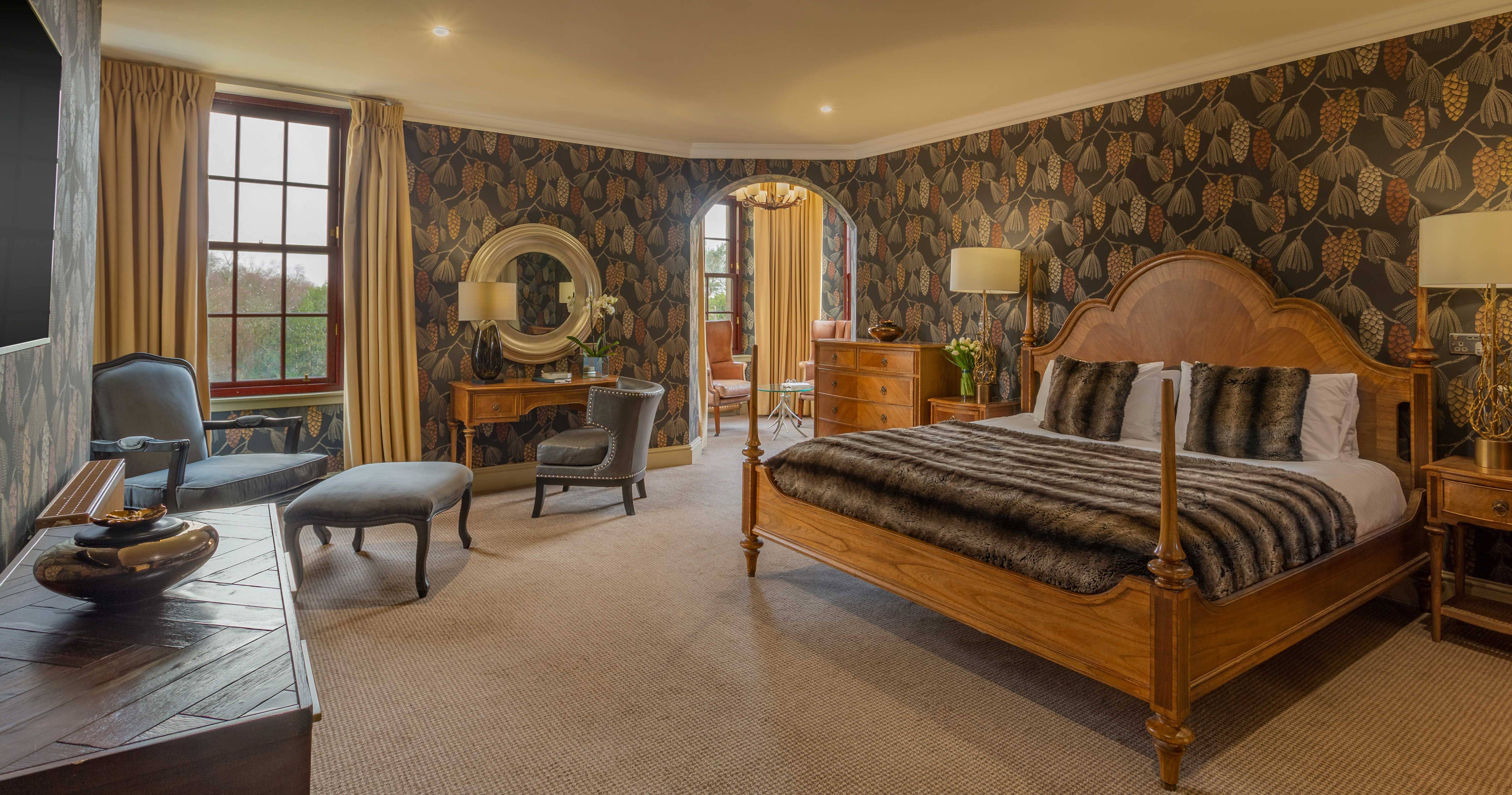 Hotel room at Gleddoch Imperia Spa with pinecone wallpaper, large wooden bed, two armchairs, and a small sitting area.