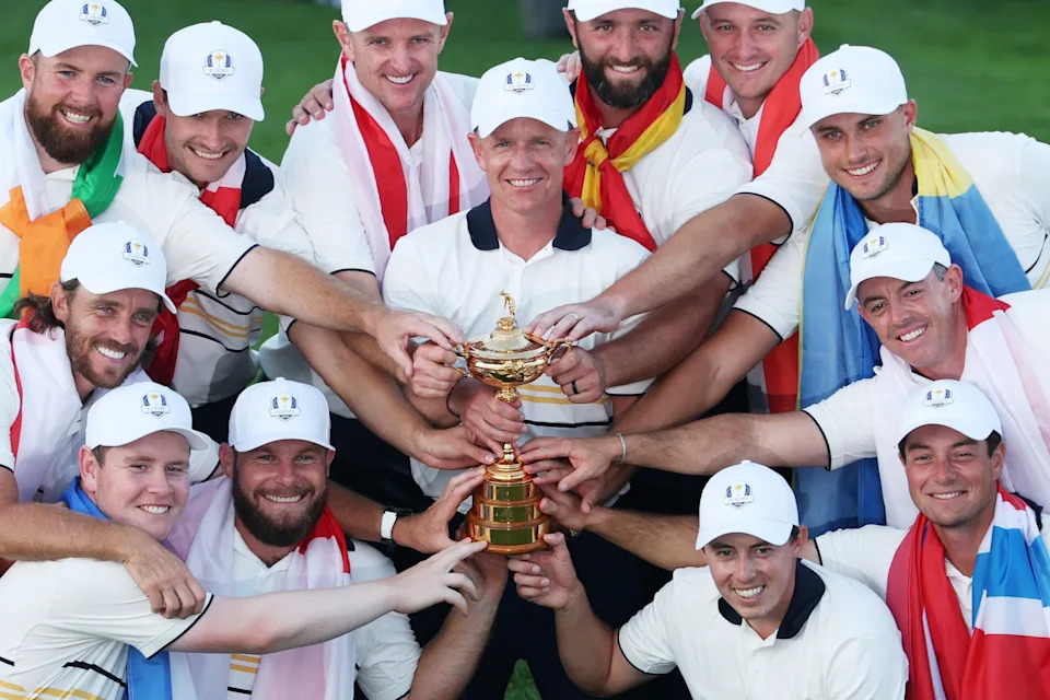 Group of golfers in matching outfits celebrate holding a trophy, each wearing caps and striped shirts, with flags draped around their shoulders