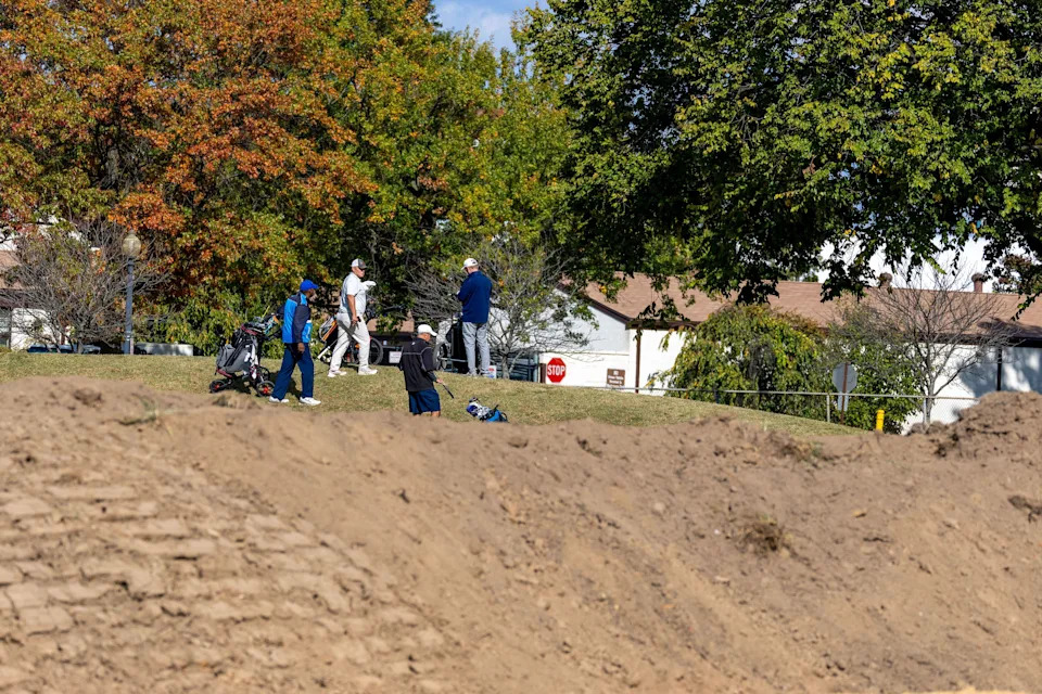 Golfers play hole six as trucks unloads debris. / Tasos Katopodis / Getty Images