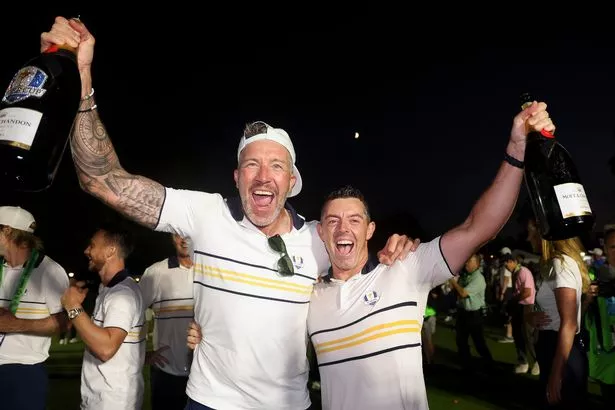 Ian Finnis, caddie of Tommy Fleetwood (Not Pictured), and Rory McIlroy of Team Europe celebrate with champagne after Team Europe defeated Team United States 15-13 during the Sunday singles matches of the 2025 Ryder Cup at Black Course at Bethpage State Park Golf Course on September 28, 2025