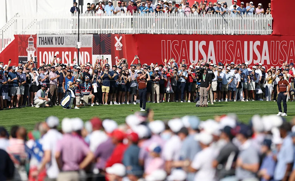 Crowd at a golf event on Long Island, with banners saying "USA" and "Thank you," watching players on the course