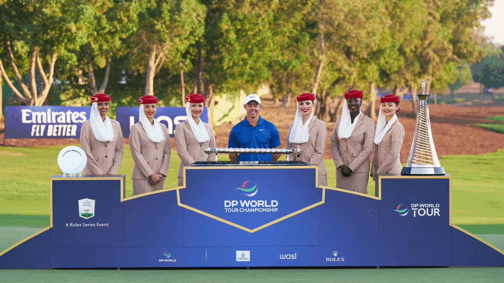 DP World Tour Championship Prize Money Payout 2025 Rory McIlroy stands behind the DP World Tour Championship and the Race To Dubai trophies with six Fly Emirates flight attendants alongside him in 2024