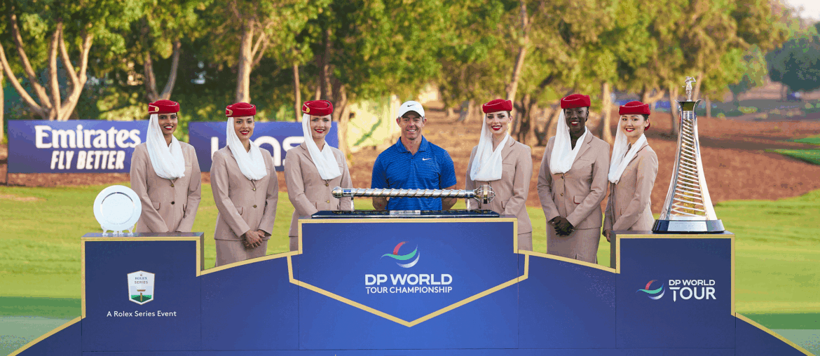 Rory McIlroy stands behind the DP World Tour Championship and the Race To Dubai trophies with six Fly Emirates flight attendants alongside him in 2024