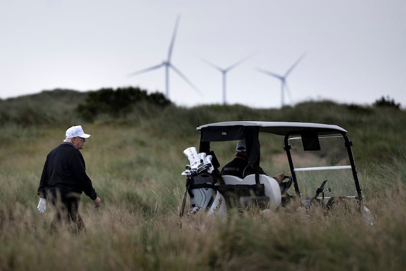 US President Donald Trump (L), backdropped by Turbines at the European Offshore Wind Deployment Centre, also known as the Aberdeen Bay Wind Farm, walks on the first fairway after playing off the first tee to officially open the Trump International Golf Links course in Balmedie, Aberdeenshire, north east Scotland on July 29, 2025. (Photo by Brendan Smialowski / AFP) (Photo by BRENDAN SMIALOWSKI/AFP via Getty Images)