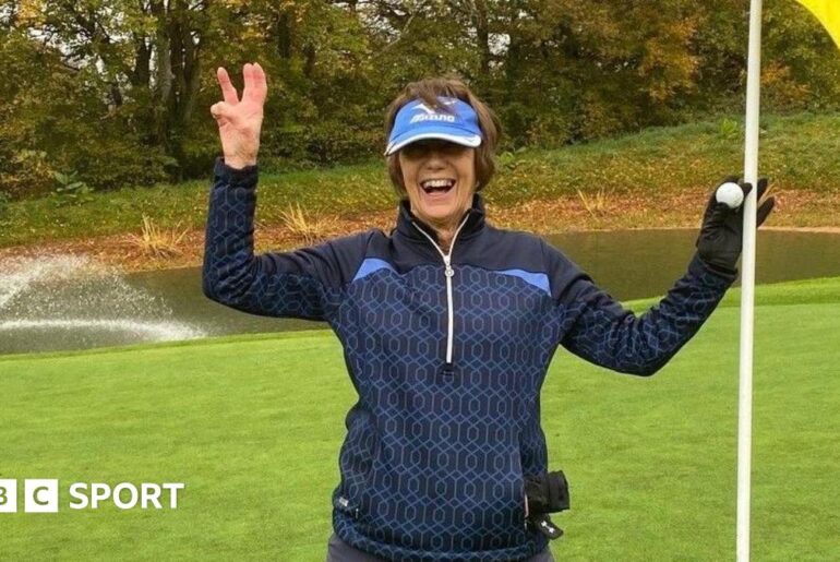 Lyn Parry holds up three fingers and a flag to celebrate her hole-in-one treble success