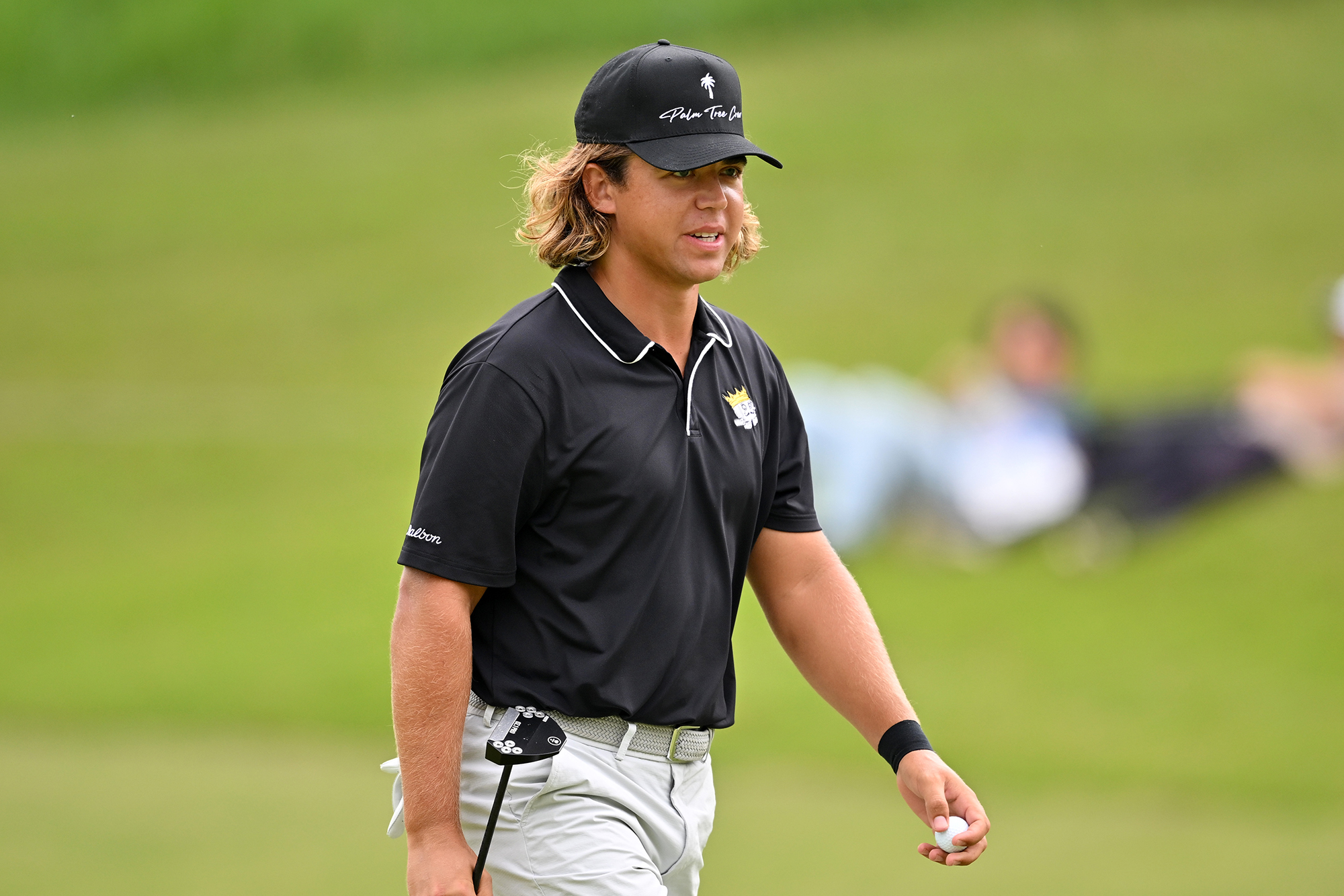 Garrick Higgo walking on a golf course holding the golf ball in his left hand and the putter in his right hand
