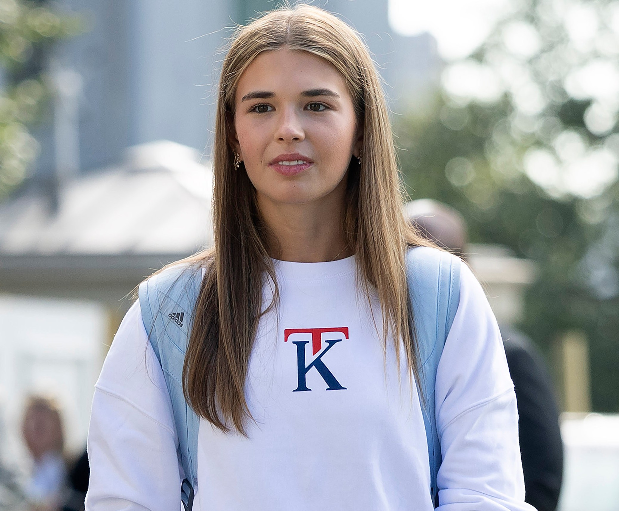 Kai Trump wearing a white sweatshirt with a red "T" and blue "K" logo.