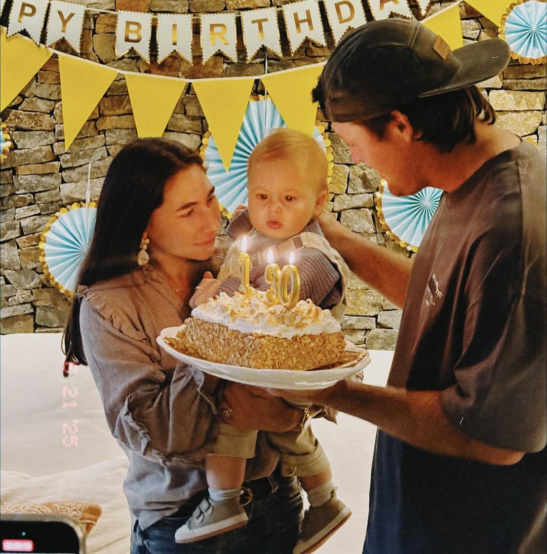 Parents holding their baby with a birthday cake and lit candles.