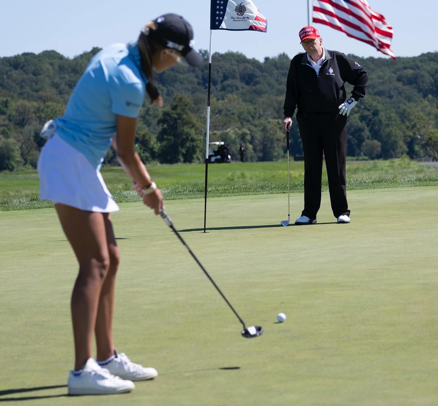 Kai Trump putting on a golf course while Donald Trump watches.
