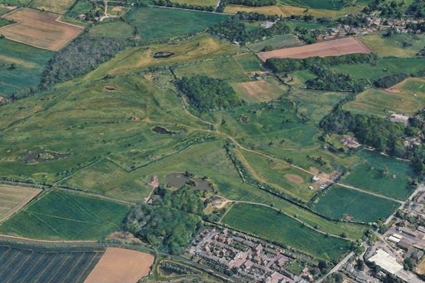 A satellite image show a golf course surrounded by countryside on one side and housing on the other.