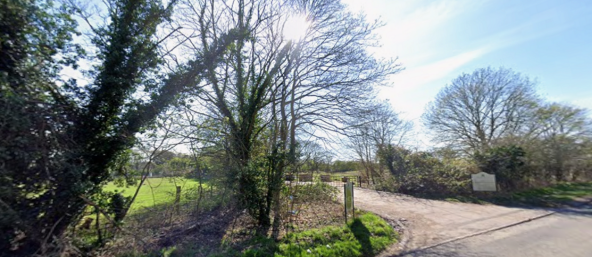The entrance to a closed golf course, showing a driveway surrounded by trees.
