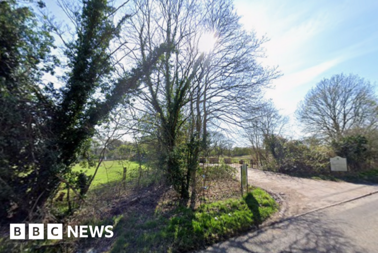 The entrance to a closed golf course, showing a driveway surrounded by trees.