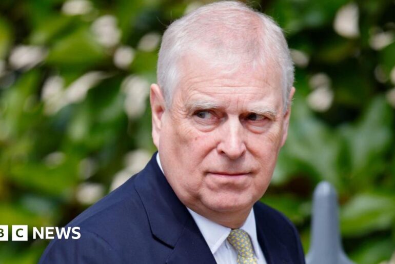 Image of Andrew Mountbatten Windsor. He is looking off to the right. Andrew has thinning grey hair and is wearing a navy suit jacket, white shirt and a yellow patterned tie