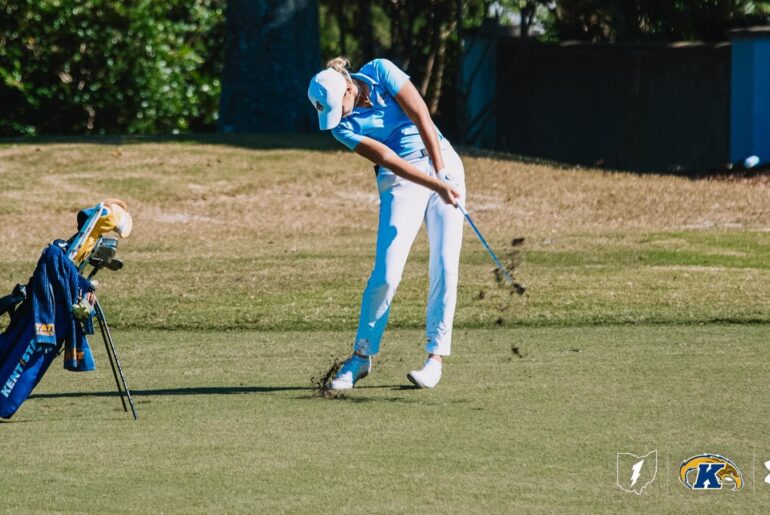 Veronika Kedronová stands smiling in front of a Kent State Golden Flashes backdrop, holding her invitation to the Augusta National Women’s Amateur. The open invitation folder displays the official Augusta National crest and printed invitation inside.
