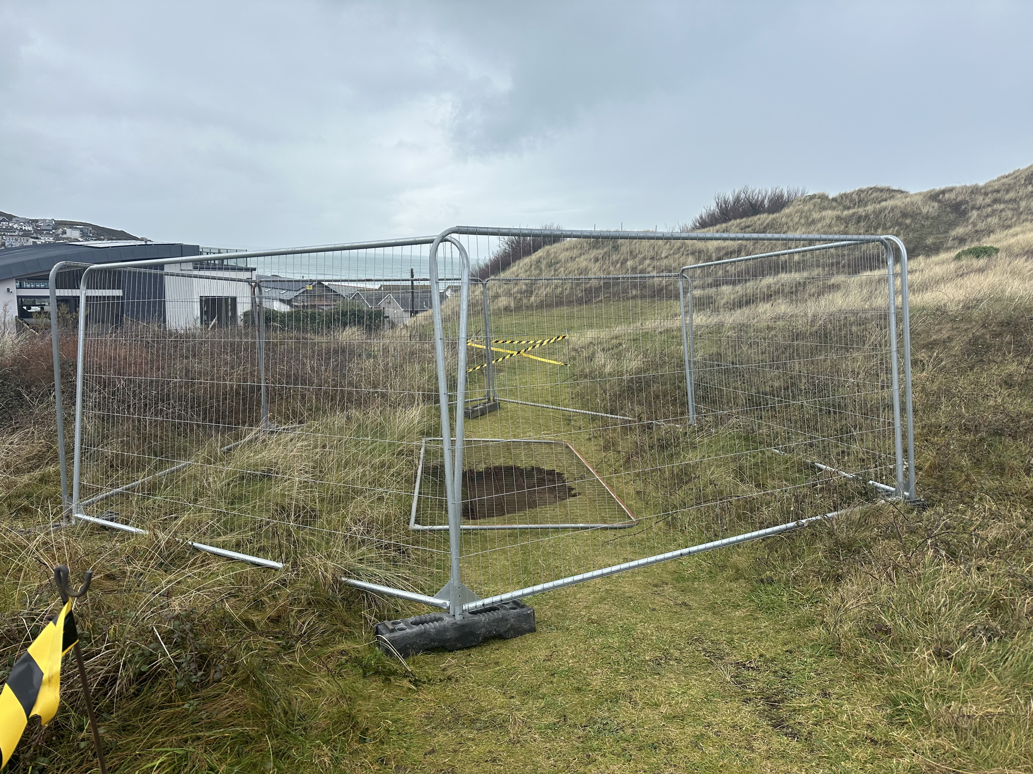 A large shaft in the ground at Perranporth Golf Club, fenced off with temporary metal barriers.