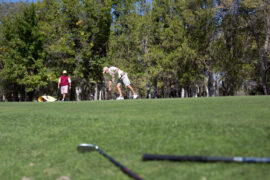 Image of four golfers in the distance, close up of golf clubs on the ground