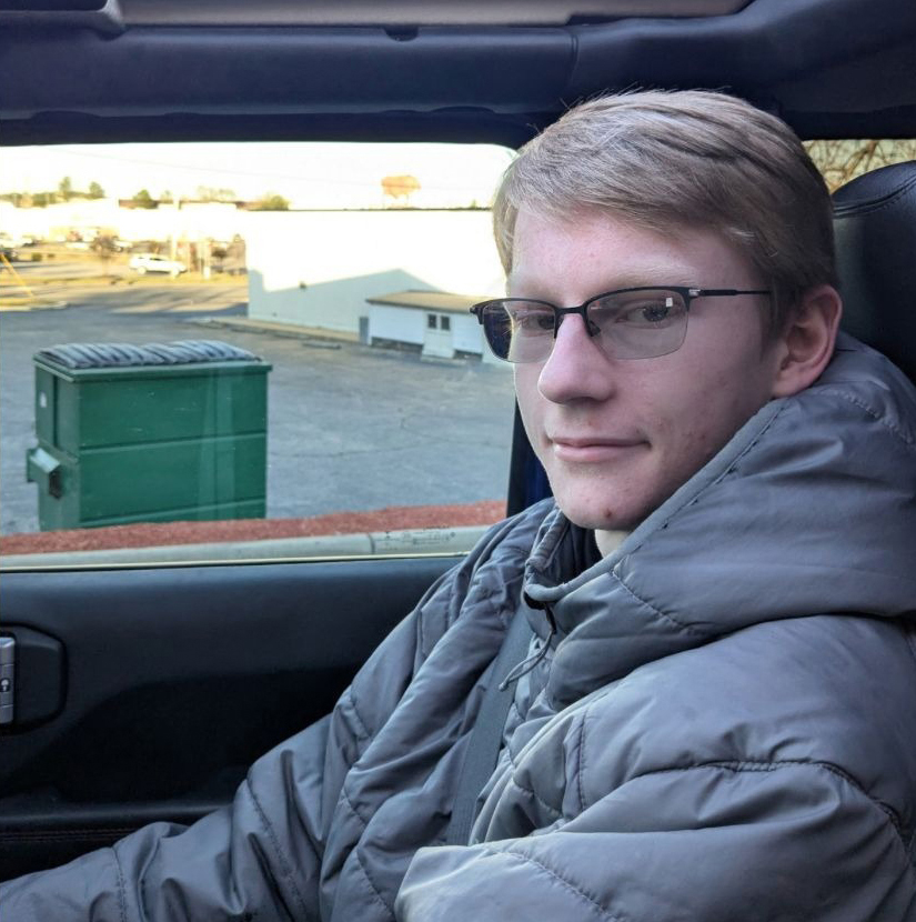 Austin Tucker Martin, a young man with glasses and a gray puffer jacket, in a car.