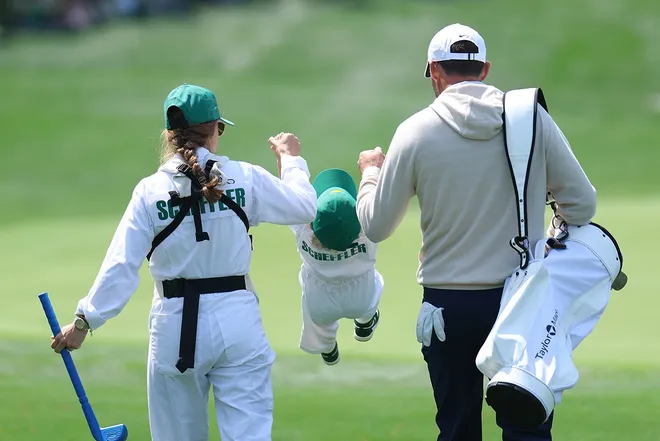 Meredith Scheffler and Scottie Scheffler swing son Bennet in the air as they walk the sixth hole during the Par 3 Contest prior to the 2026 Masters Tournament at Augusta National Golf Club.
