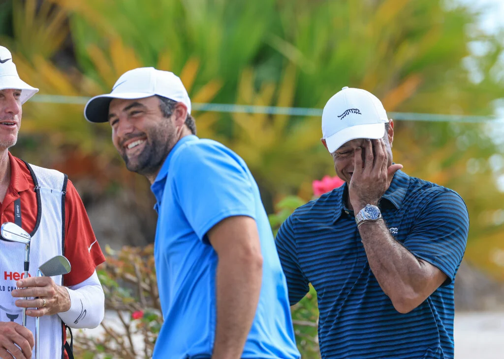 Tiger Woods of The United States enjoys a light-hearted moment whilst watching Scottie Scheffler of The United States on the 17th hole as Scheffler's caddie Ted Scott.